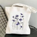White canvas tote bag featuring an artistic blue cornflower print on a metal chair - Blue Cornflower