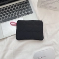 Close-up of black quilted mini pouch with heart patterns and pink strap on a desk - Black Heart