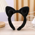 Detail of plush black cat ear headband with soft pom-poms on a rustic wooden desk - Black