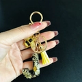 Detailed close-up of resin letter J keychain with real dried flowers, bee charm and yellow tassel - Letter J