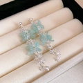 Gros plan de boucles d'oreilles fleurs bleu clair avec chaînes argentées sur boîte beige - Boucles d'oreilles pampilles argentées pétale bleu clair