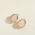 Detail view of teardrop earrings with golden frames and pink stone inlay on beige background - White Turquoise