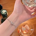 Silver chain bracelet with sparkling Saturn heart charm worn by a model holding a glass - Heart Zirconia Adjustable Slider Bracelet / Silver
