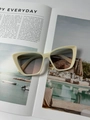 Primer plano de gafas de sol cat-eye color crema sobre una revista de moda elegante - Marco Beige Lentes Degradados Azul Rosa