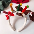 Dettaglio del cerchietto di Natale con fiocco rosso, renna e decorazioni festose in peluche - Renna Bianca