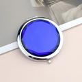 Portable round metal compact mirror with faceted blue gemstone inlay on a pink surface - Crystal Deep Blue