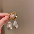 Macro shot of gold irregular metal earrings with baroque pearl charms held by hand - Gold Irregular Pearl Drop