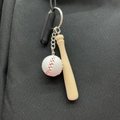 Miniature baseball bat and ball keychain accessory hanging on a black textured backpack - White
