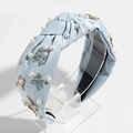 Detail of light blue fabric headband with knotted design, white pearls, and enamel bows - Sky Blue