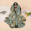 Eleganter salbeigrüner Satinschal mit Magnolien-Print, drapiert auf einer Ledertasche - Grün