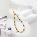 Close-up of beaded phone strap with amber gold beads and star charms on white texture - Brown