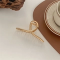 Dettaglio di una grande pinza per capelli in metallo dorato con design a spirale su tavolo - Oro