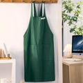 Cross-back dark green cotton linen apron with large front pocket hanging on a rack - Green