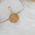 Handmade camel wool yarn ball ornament with loop hanging on a white plush background - Khaki