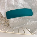 Close-up of a teal padded hair clip with twill texture in a white metal wire basket - Peacock Green