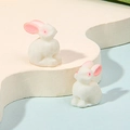 Close-up of two miniature white resin rabbits on a cream wavy stand with light blue backdrop - Sitting White Rabbit