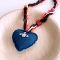 Detail of a denim heart pendant with a silver saturn ring logo and braided cord necklace - Heart Pendant (WN1692) / Black-Red-Blue Rope