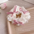 Dettaglio di scrunchie in organza bianca con fiocchi di nastro rosa su un vassoio beige - Bianco Organza Fiocco