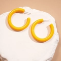 Close-up of bright yellow C-shaped acrylic earrings with polished finish and silver posts - Yellow