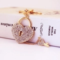 Golden heart lock and key keychain with sparkling rhinestones on a white book surface - White