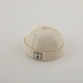 Dettaglio del berretto docker beige con trama in tela e toppa in pelle con lettera S - Etichetta Lettera S - Bianco Sporco