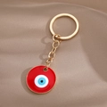 Detail eines goldenen Evil Eye Schlüsselanhängers mit rotem Emaille auf Stoffhintergrund - Gold Rotes Rundes Auge