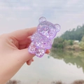 Detail of purple glitter bear phone grip stand held against a scenic lake background - Expanding Stand / Purple Glitter Bear