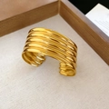 Detail of a wide gold metal cuff bracelet with layered wavy textures on a wooden tray - Gold Multi-layer Linear