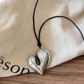 Macro view of polished silver heart pendant with adjustable black cord on linen texture - Silver