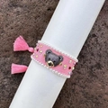 Detailed view of a pink woven bracelet with a rhinestone-encrusted bear and tassels - Pink