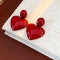 Close-up of minimalist glossy red heart-shaped earrings on a vintage textured book - Red