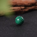 Polished 16mm malachite stone sphere with deep green stripes on a black textured surface - Malachite