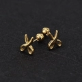 Detail view of golden scissor-shaped titanium steel ear studs on a black textured surface - Scissors / Gold