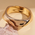 Nahaufnahme eines breiten goldenen Wellenarmreifs auf einem Naturstein-Display - Spiralform / Gold