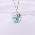 Detail of round gold pendant with blue dried flowers and butterfly in resin - Gold Blue
