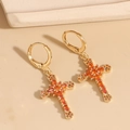 Gold-plated cross earrings with orange and amber zircons on a beige surface - Brown