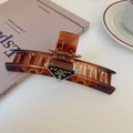Amberkleurige haarklem van acetaat met driehoekig logo op witte tafel met koffie - 10# Haarklem-Koffie