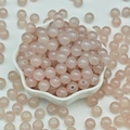 Detailed view of translucent light pink round glass beads in a white flower-shaped bowl - 4mm / Fruit Pink