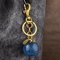 Blue glitter apple keychain with gold metal ring and hook on grey fabric background - Blue