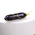 Blue sandstone hexagonal pendant wrapped in gold wire on a white display base - Blue Sandstone