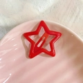 Macro shot of a glossy red star hair clip on a pink shell plate with white lace details - The Star-Red