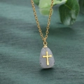 Vue détaillée d'un pendentif en pierre avec croix dorée sur fond de bois vert foncé - Gris