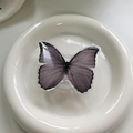 Close-up of a grey gradient butterfly expandable phone stand on a white ceramic tray - Black Purple Gradient Butterfly