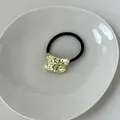 Elastic hair tie featuring a textured gold geometric metal charm with a black band - Asymmetric Wave Gold