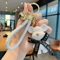 White knitted bear keychain with black bow and golden bell on a white braided wristlet - Knit Bear-White