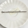 Detailed macro view of silver polished nail-shaped brooch with textured head on white dish - 42 Silver Nail (Z-1282)
