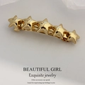 Golden spring hair clip with five stars design on a textured gray background - Gold Hammered Star Clip