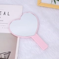 Detailed view of pink heart-shaped handheld makeup mirror on a soft white plush rug - Pink