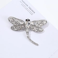 Detailed close-up of a silver dragonfly brooch with sparkling crystals on a magazine page - 9.1*7cm / White