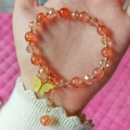Detailed shot of beaded bracelet with orange beads and yellow butterfly charm on wrist - Tan
